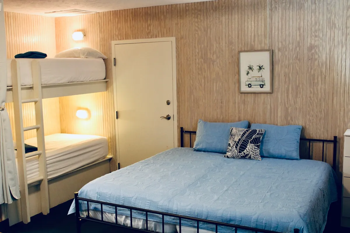 This image showcases a relaxed and inviting studio space featuring both a bunk bed and a queen bed, with decorative wall art adding character. The cozy sleeping setup is ideal for families or couples, conveying comfort and versatility. The beds are centrally located within a compact, open layout, illustrating how sleeping and lounging areas can be blended in an efficiency studio.