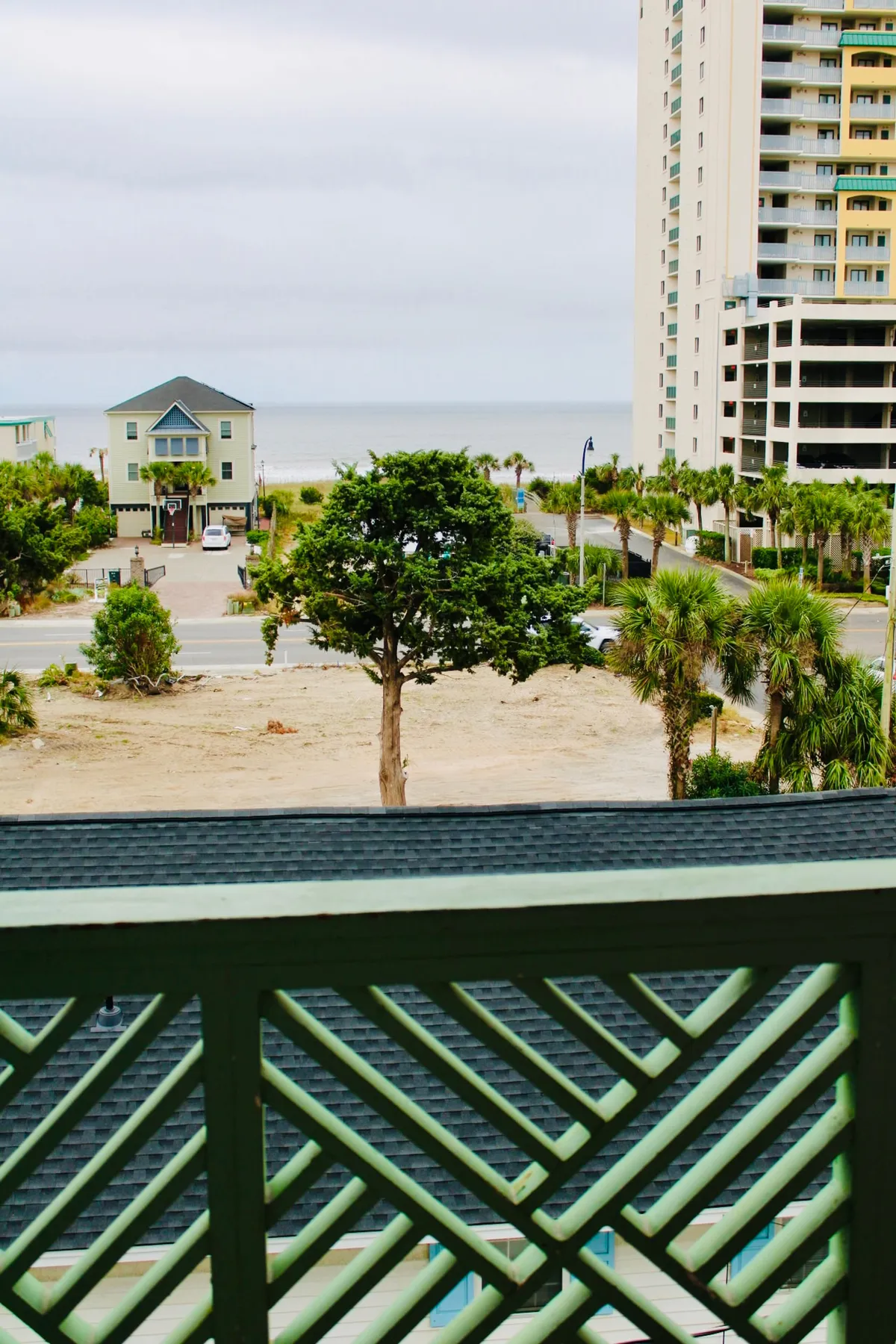 The hero image features a charming balcony with a vibrant green railing overlooking swaying palm trees, a nearby classic beach house, and an expansive ocean view. The golden light of sunset bathes the scene, creating a tranquil, inviting atmosphere that suggests relaxing moments outdoors.